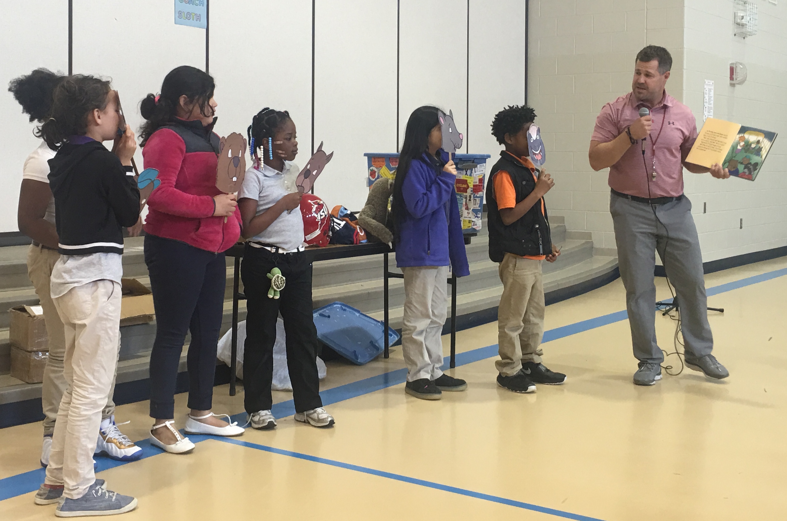 5 kids holding masks and 1 adult reading a book