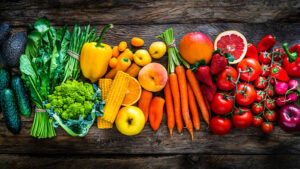 Top view of a large assortment of healthy fresh rainbow colored organic fruits and vegetables arranged side by side on rustic wooden table. 