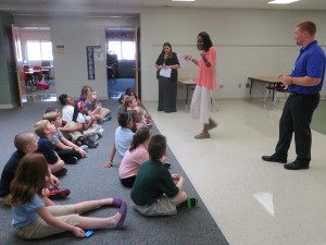 two rows of elementary students sitting and listening to three teachers talk in a pod area