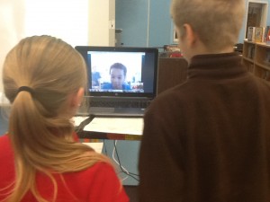 Two fourth grade students talking to another student through a computer