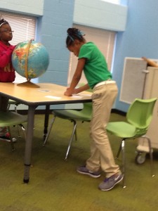 Two girls looking at a globe, writing down answers