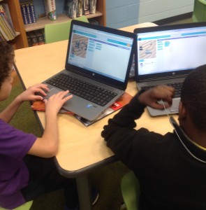 Two upper elementary students coding on their laptops