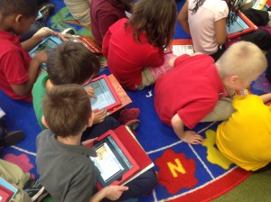 A group of kindergarten students looking at their red iPads learning how to computer code
