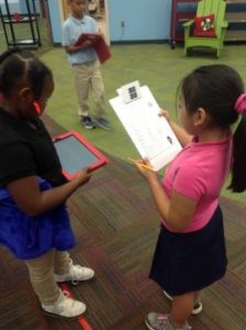 Students using an iPad to scan QR codes. One is holding a clipboard. The other is holding the iPad